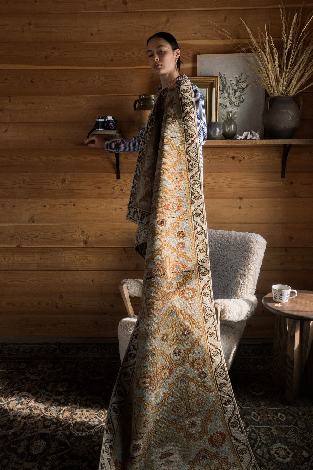 Model on chair holding one-of-a-kind vintage rug custom sourced by District Loom in cabin setting